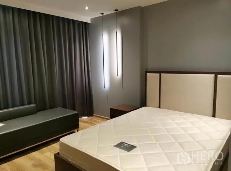Condominium for rent in Sathon, Bangkok - Bedroom corner with padded headboard, daybed and tall pendant lights against dark curtains.