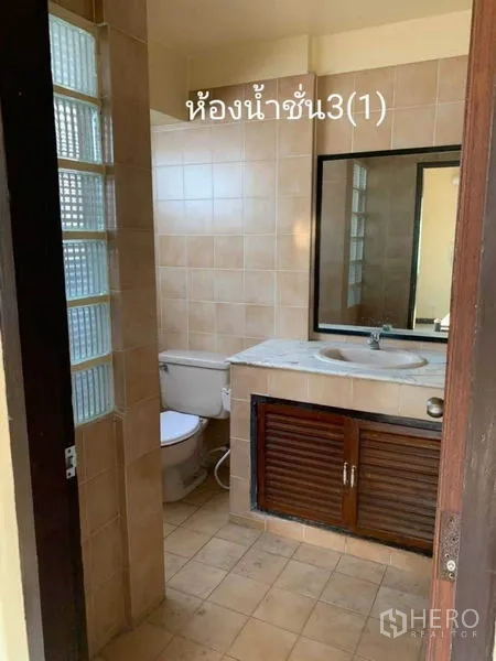 Townhouse for rent in Phra Khanong, Bangkok - Bathroom with beige tiles, glass-block partition, vanity, and toilet.
