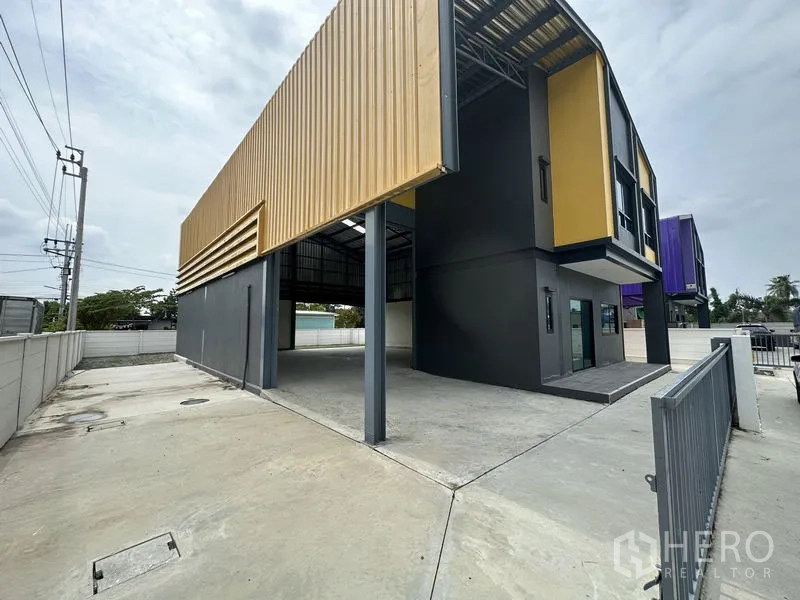 Factory for rent or sale in Bang Yai, Nonthaburi - Side view showing covered loading bay, gated entrance and wide concrete yard.