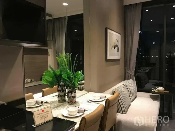 Condominium for rent in Watthana, Bangkok - Cozy dining nook with a marble table, green centerpiece, and sofa beside floor-to-ceiling windows at night.