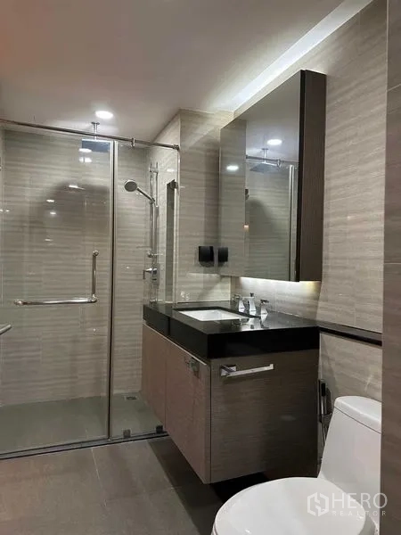 公寓 出售在Pathum Wan, Bangkok - 现代浴室，玻璃淋浴间与带灯洗手台和大镜子。