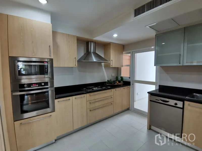 Condominium for rent in Khlong Toei, Bangkok - Fully fitted kitchen featuring built-in oven and microwave, gas cooktop, range hood, and light wood cabinetry.
