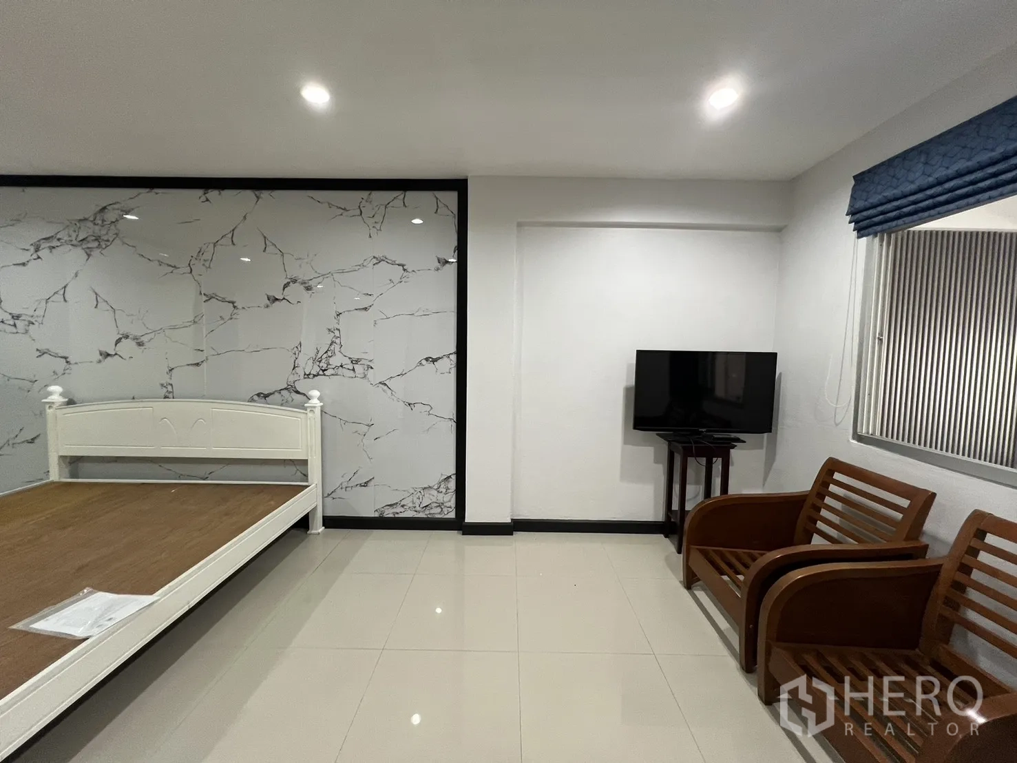 联排别墅 for rent in Watthana, Bangkok - 卧室一角，石纹墙面、电视与木质休闲椅。