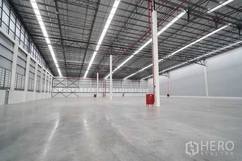 Warehouse for rent in Khlong Luang, Pathum Thani - Wide open warehouse space with columns, fire hose cabinets, side louvered windows, and cross-braced end wall.
