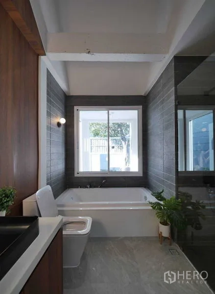 Townhouse for rent in Watthana, Bangkok - Contemporary bathroom featuring soaking tub, gray wall tiles, window and glass shower.