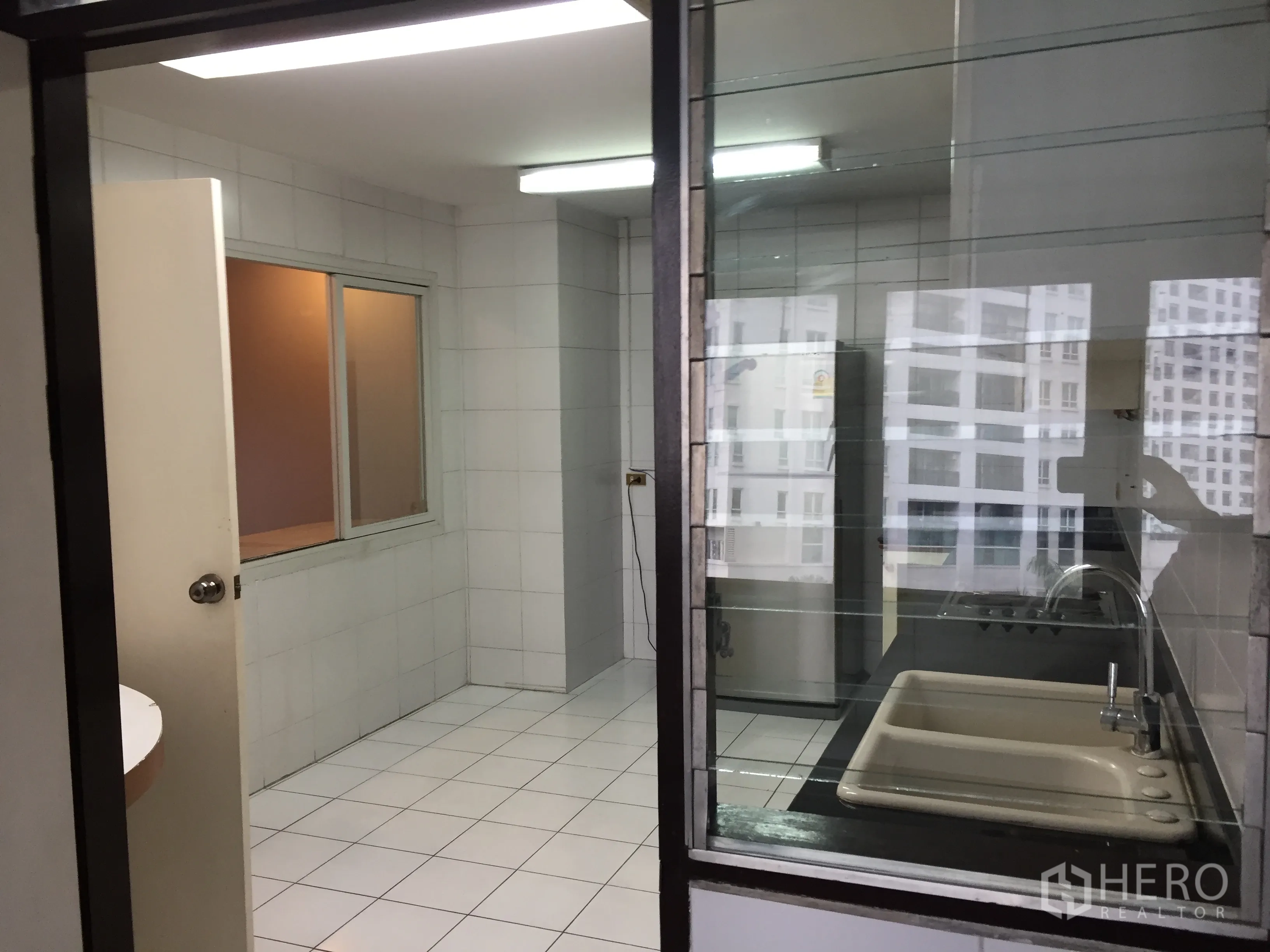公寓 出租在Watthana, Bangkok - 厨房与生活阳台以玻璃分隔，可见市景倒影，近娜娜BTS