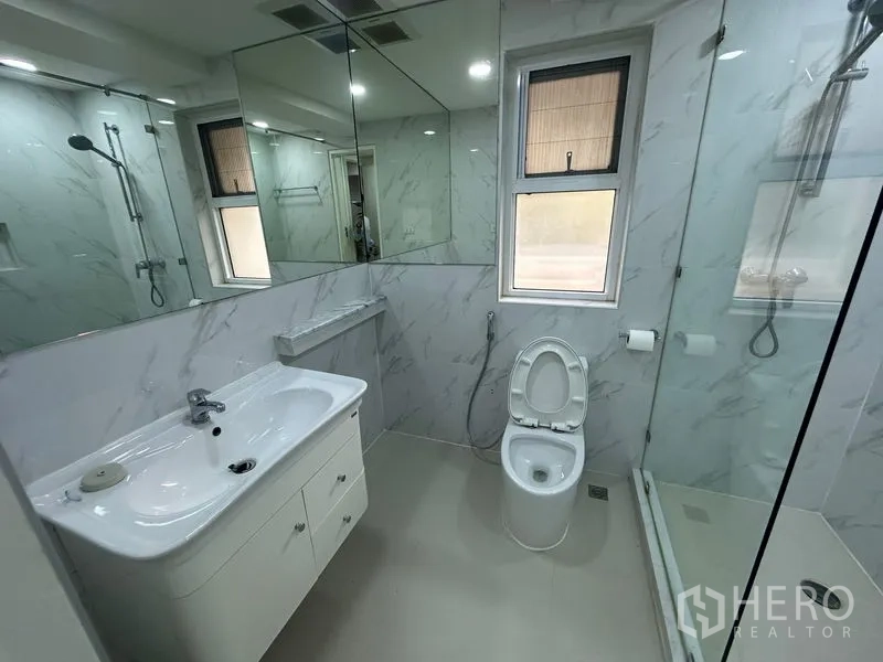 Condominium for rent in Watthana, Bangkok - Bright bathroom with window, glass shower, mirrored cabinets and vanity.