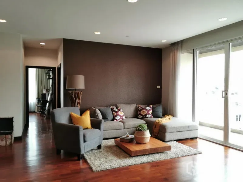 Condominium for rent or sale in Khlong Toei, Bangkok - Bright living room with L-shaped gray sofa, wood floors, coffee table, and sliding glass doors to a balcony.