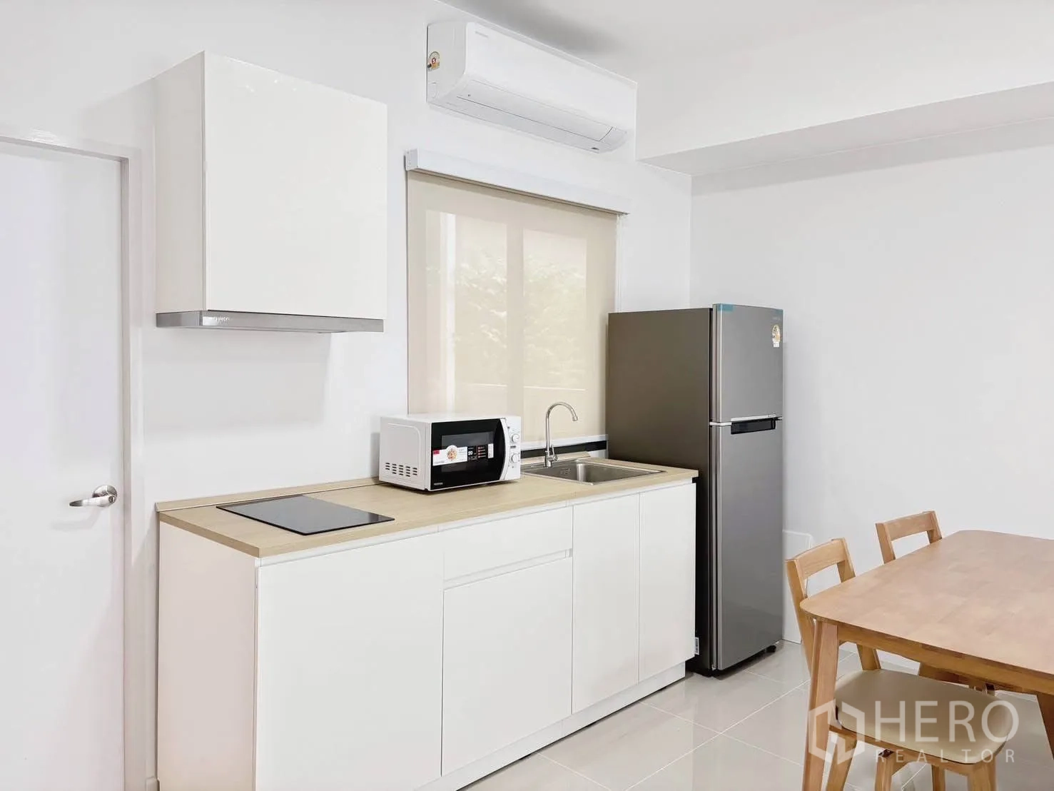 Townhouse for rent in Bang Phli, Samut Prakan - Compact white kitchen with cooktop, microwave, sink, and stainless-steel fridge next to dining table.