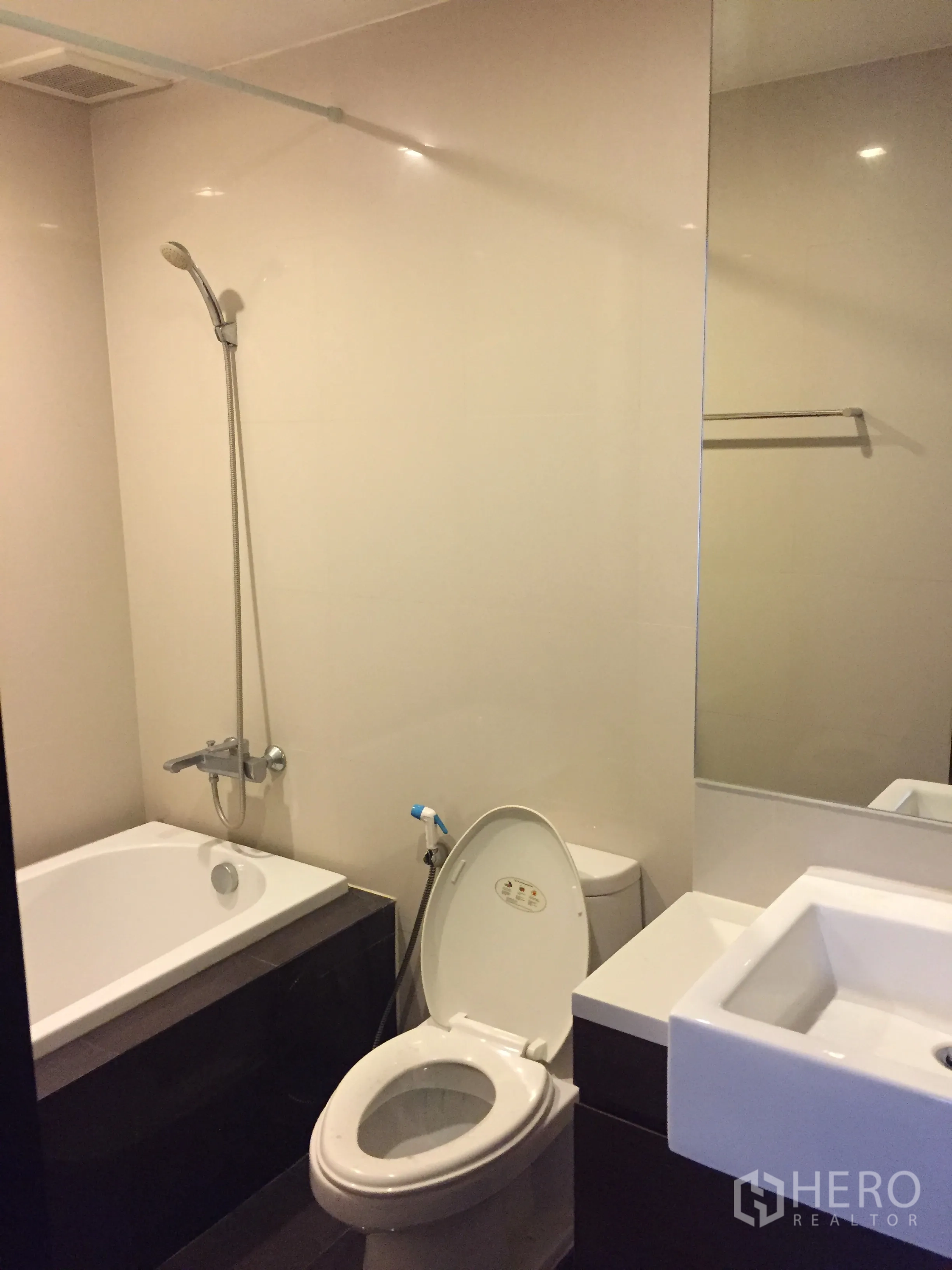 Condominium for rent in Khlong Toei, Bangkok - Modern bathroom featuring a bathtub with handheld shower, square vanity, and toilet.