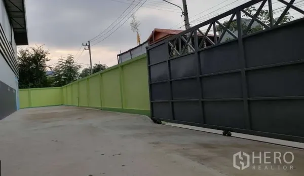 Warehouse for rent in Mueang Samut Sakhon, Samut Sakhon - Driveway and sliding steel entrance gate with high green perimeter wall for secure truck access.