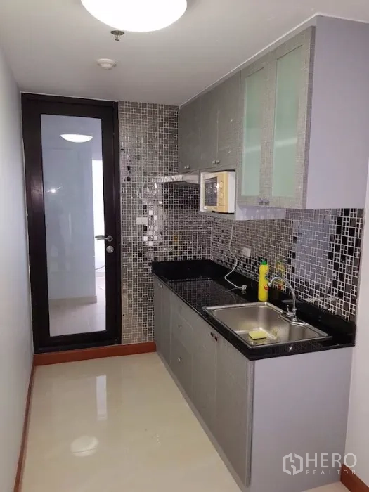 Condominium for rent in Watthana, Bangkok - Closed galley kitchen with mosaic backsplash, black countertops, upper cabinets and sink, door to service area.