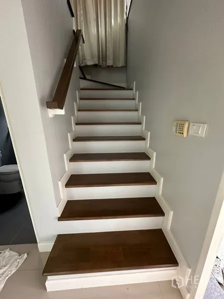 Detached House for rent or sale in Lam Luk Ka, Pathum Thani - Wood-tread staircase with white railing and a wall-mounted security keypad.
