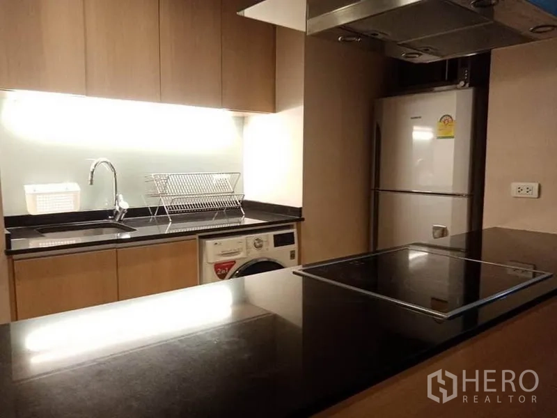Condominium for rent in Sathon, Bangkok - Close view of sleek kitchen island, sink and backsplash with electric cooktop and extractor.