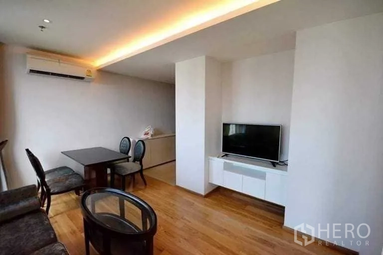 Condominium for rent or sale in Phra Khanong, Bangkok - Open-plan living and dining area with TV wall unit, wood flooring and cove lighting.