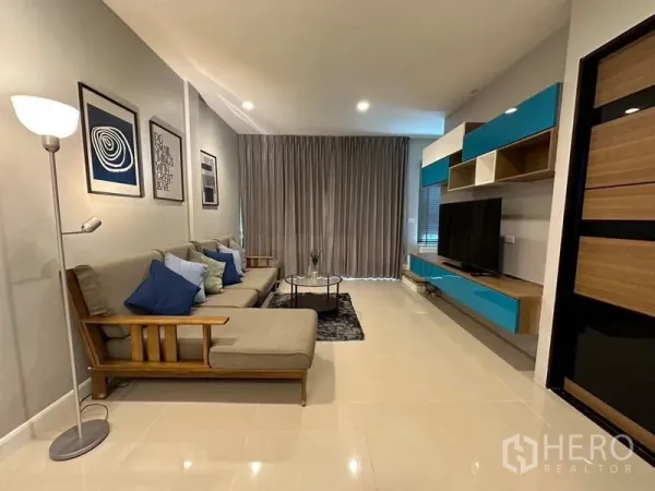 联排别墅 出租在Chom Thong, Bangkok - 客厅另一角度，转角沙发、电视墙柜与落地窗帘