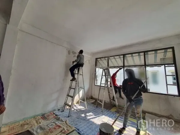 Shophouse for rent in Bangkok - Spacious room with long horizontal windows and ladders, surfaces prepared for renovation.