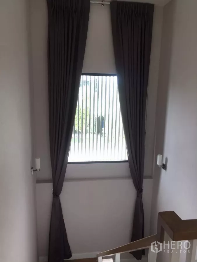 独立式住宅 出租在Samut Prakan - 楼梯平台高窗配长窗帘，引入自然光。