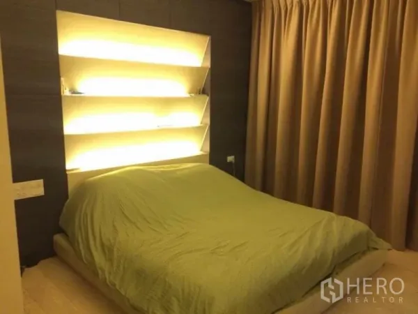 Condominium for rent in Watthana, Bangkok - Bedroom with platform bed, illuminated wall shelves, and floor-to-ceiling curtains.