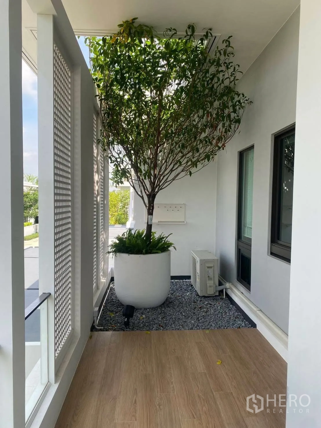 Detached House for rent or sale in Bang Phli, Samut Prakan - Covered terrace with wood-look flooring, white lattice screen, and a large potted tree.