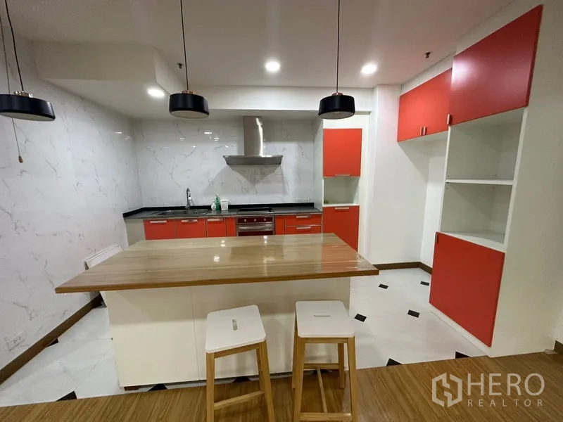 Condominium for rent in Watthana, Bangkok - Open kitchen with red cabinetry, island bench, pendant lights and stainless hood.
