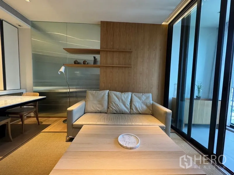 Condominium for rent in Khlong Toei, Bangkok - Cozy living room with sofa, floating shelves and sliding glass doors to the balcony.