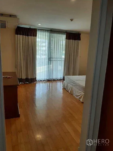 Apartment for rent in Watthana, Bangkok - Sunny bedroom with wood flooring, sheer drapes over large windows, and a queen-size bed.