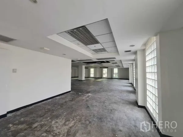 Office Space for rent in Ratchathewi, Bangkok - Bright open office with concrete floor, suspended lighting, multiple pillars, and a long row of glass-block windows near BTS Ratchathewi.