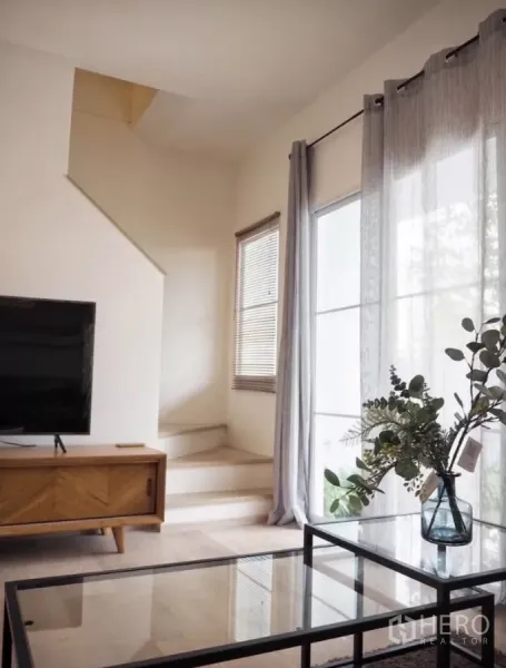 Townhouse for rent in Bang Phli, Samut Prakan - Cozy lounge area with TV console, glass coffee table and staircase beside floor-to-ceiling curtains.