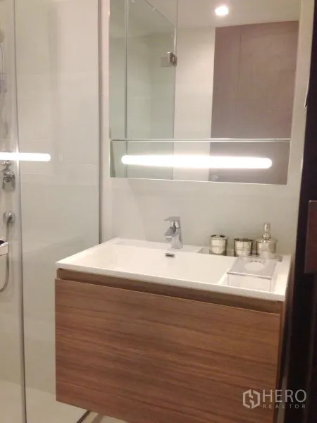 Condominium for rent in Khlong Toei, Bangkok - Contemporary bathroom with glass shower, wall-mounted vanity and large mirror.