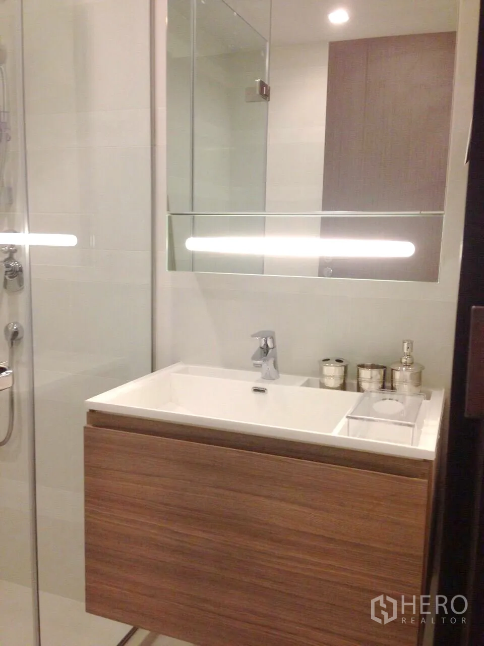 Condominium for rent in Khlong Toei, Bangkok - Contemporary bathroom with glass shower, wall-mounted vanity and large mirror.