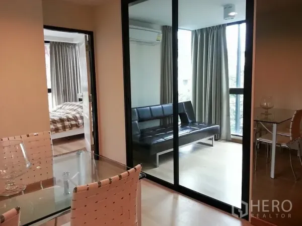公寓 出租或出售在Chatuchak, Bangkok - 玻璃推拉门分隔的采光多功能房，内有黑色沙发并邻接卧室。