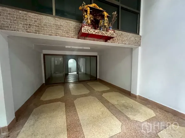 Shophouse for rent in Khlong Toei, Bangkok - Ground-floor entry hall with stone-pattern floor, brick accent wall and glass sliding partition.