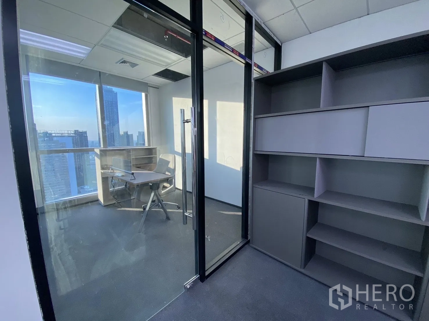 Office Space for rent in Huai Khwang, Bangkok - Glass-partitioned private office with built-in shelves, desk and skyline view through large windows.