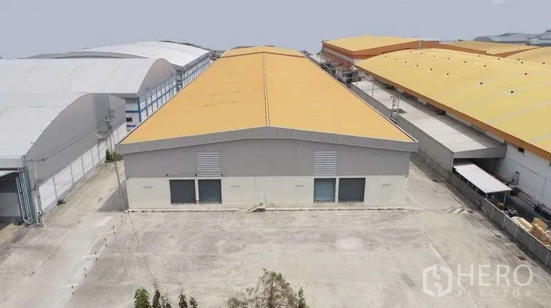 Warehouse for rent in Bang Bo, Samut Prakan - Aerial view of a yellow‑roof warehouse with a wide concrete yard and loading bays in an industrial park.