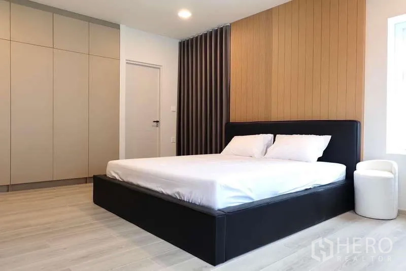 บ้าน ให้เช่าในBang Phli, Samut Prakan - ห้องนอนใหญ่ เตียงคิงส์ไซส์ ผนังหัวเตียงไม้ และตู้เสื้อผ้าบานสูง