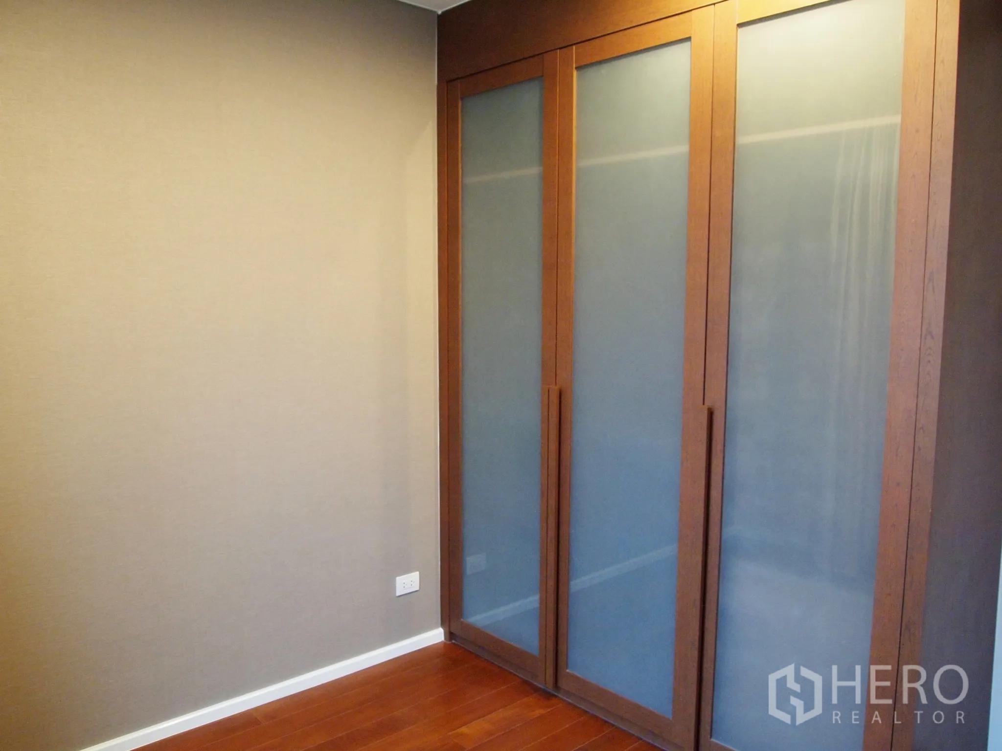 Condominium for rent or sale in Watthana, Bangkok - Bedroom corner with built-in wardrobe featuring frosted sliding doors and wooden flooring.