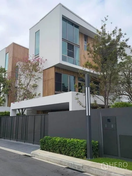 Detached House for rent in Saphan Sung, Bangkok - Modern three‑storey detached house exterior with tall windows, wood accents, gated entrance and trees.