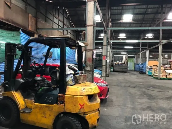 Warehouse for rent in Bang Kho Laem, Bangkok - Spacious warehouse interior with high metal roof, a forklift and parked vehicles for storage operations.