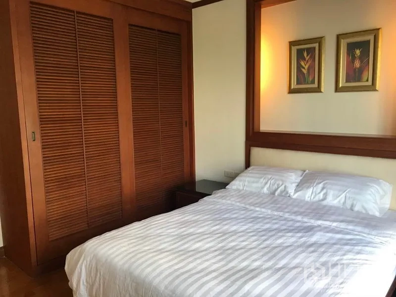 公寓 出租在Khlong Toei, Bangkok - 温馨卧室，木质嵌入式衣柜与带装饰画的双人床。