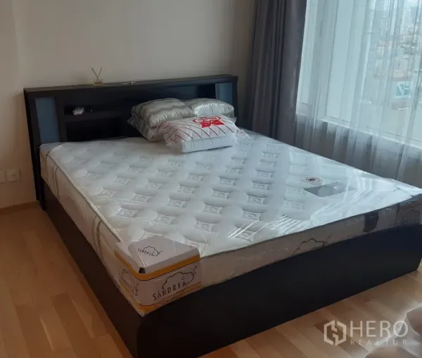 Condominium for rent in Khlong Toei, Bangkok - Bright bedroom featuring a large bed on light wood floors beside a wide window with city outlook.