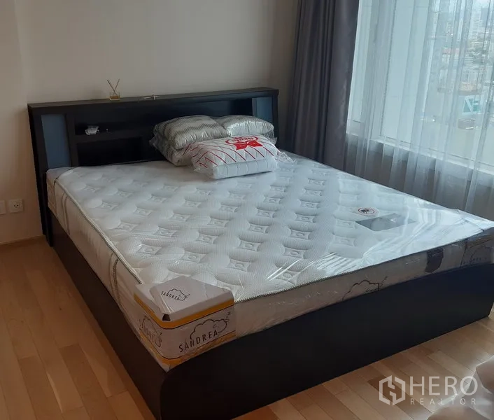 Condominium for rent in Khlong Toei, Bangkok - Bright bedroom featuring a large bed on light wood floors beside a wide window with city outlook.