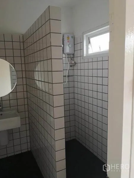 Townhouse for rent or sale in Din Daeng, Bangkok - Bathroom with white square tiles, separate shower area, small window, and a round mirror over the sink.