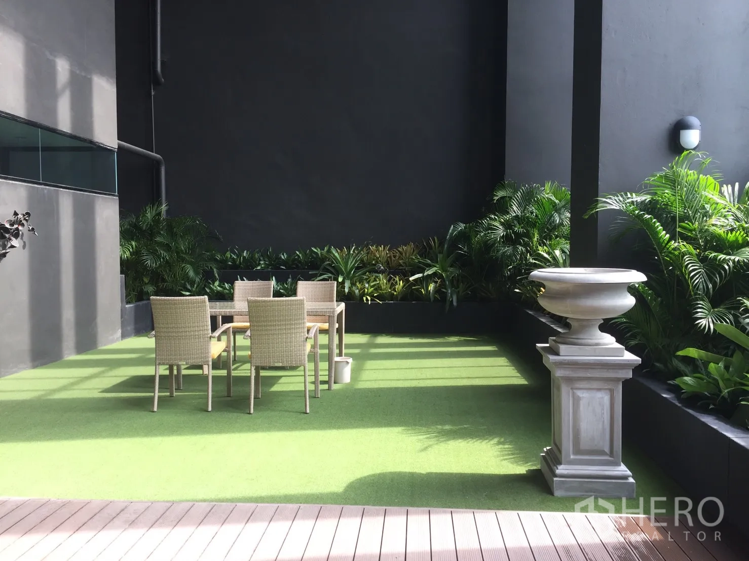 Condominium for rent or sale in Huai Khwang, Bangkok - Outdoor garden lounge with table and chairs on artificial turf surrounded by plants.