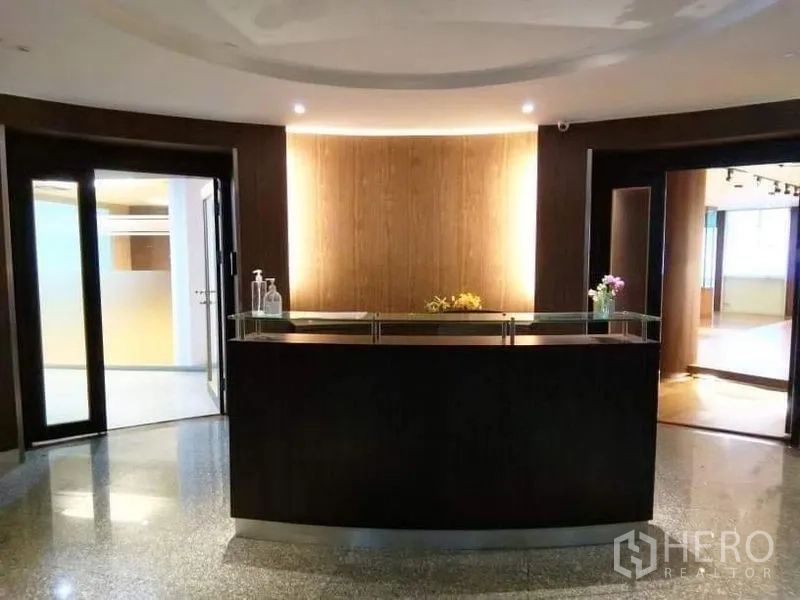 Office Space for rent - Welcoming reception lobby with curved dark-wood desk, backlit wall and polished stone floor.