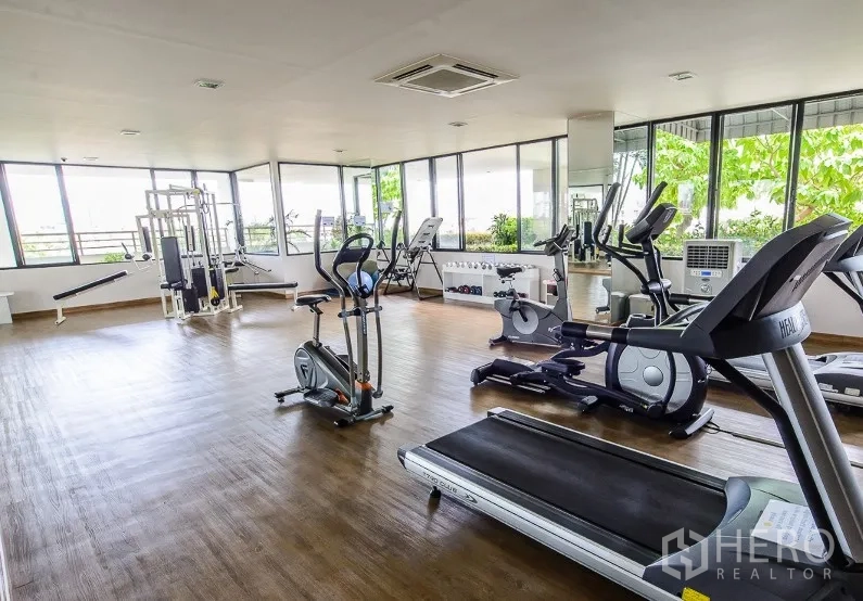 Condominium for rent in Watthana, Bangkok - Well-equipped fitness room with treadmills, exercise bikes and weight machines surrounded by windows.
