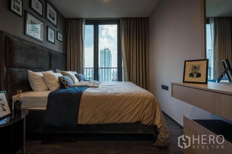 Condominium for rent or sale in Din Daeng, Bangkok - Cozy bedroom with large window overlooking the Bangkok skyline, soft curtains and a floating shelf desk.