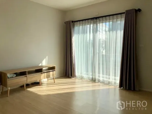Townhouse for rent in Suan Luang, Bangkok - Second-floor room with balcony access through sheer curtains and a low wooden sideboard.