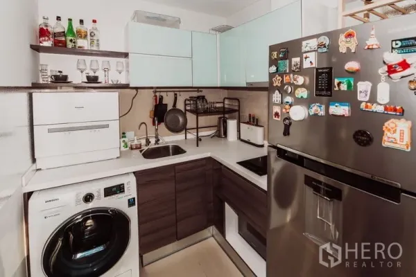Condominium for rent in Sathon, Bangkok - Compact L-shaped kitchen with modern appliances, large fridge, and washing machine.
