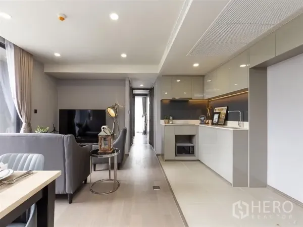 Condominium for rent in Pathum Wan, Bangkok - Open-plan living room with TV, gray sofa and sleek kitchen cabinetry in a Bangkok condo.